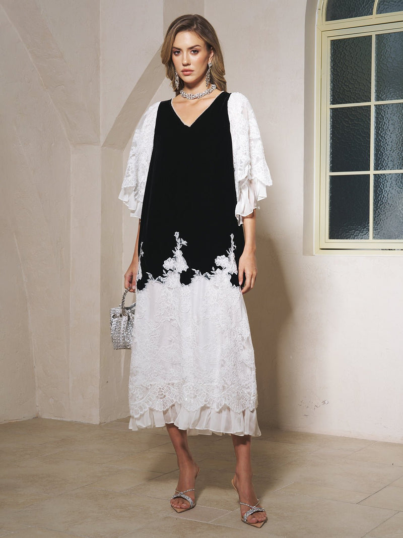 A woman stands indoors near a frosted glass window, wearing Social Queen's Pearl-Trim Silk Velvet Dress, paired with silver heels, a silver handbag, and a statement necklace.