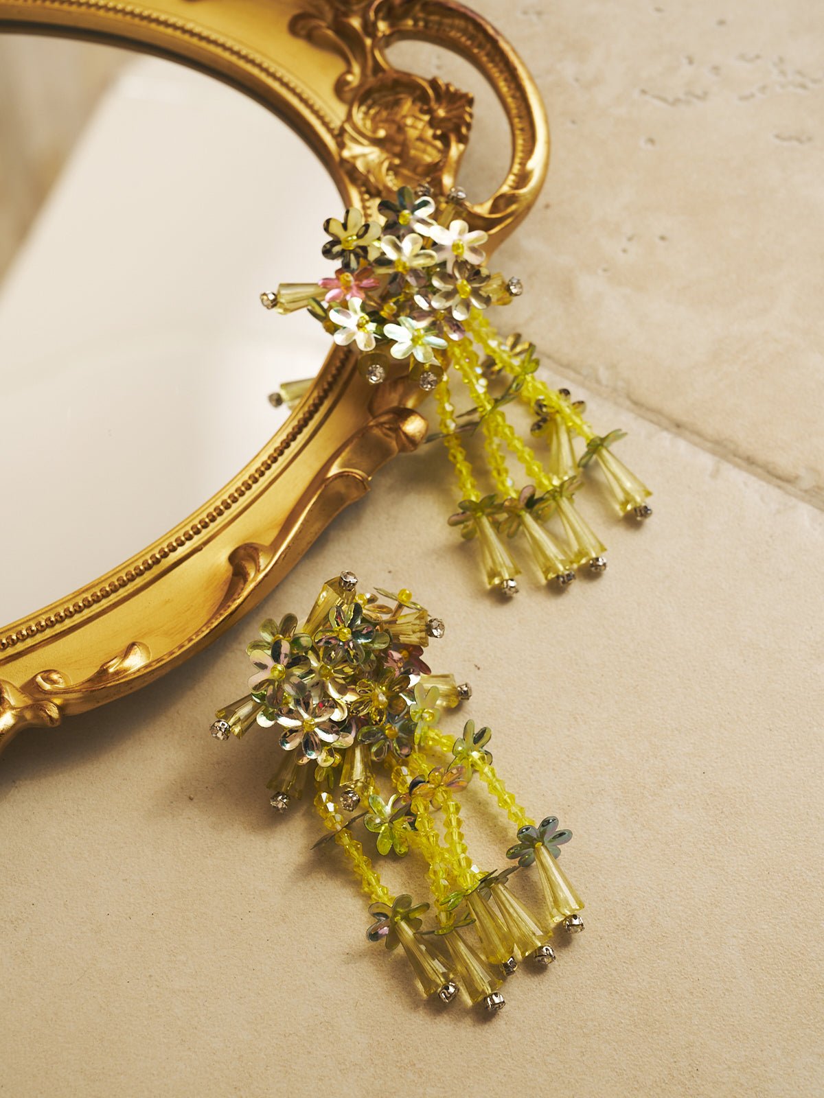 The Social Queen Petal Sequin Beaded Tassel Earrings feature handcrafted floral beads and dangling tassels, shown on a beige surface with a gold-framed mirror—an elegant choice for wedding guest jewelry.