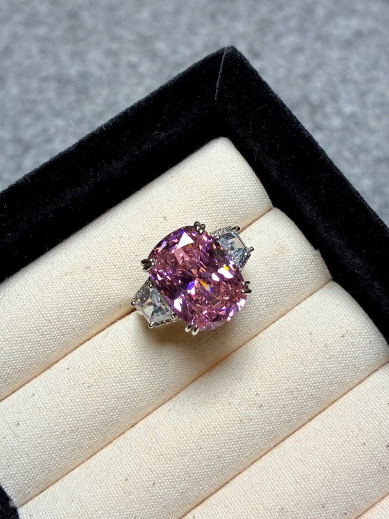 The Social Queen Pink Crystal Cushion Ring, white gold-plated with a large cushion-cut pink crystal and two triangular clear accents, is shown in a black velvet ring box.