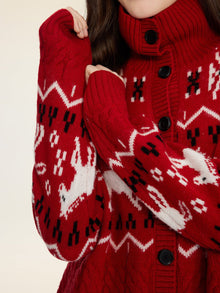 A person wears the Social Queen Playful Motif 100% Wool Cardigan, a red knit sweater with white and black reindeer and geometric patterns; only their torso and part of their face are visible.