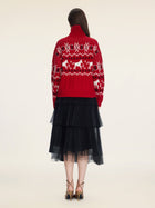 A person faces away, wearing the Social Queen Playful Motif 100% Wool Cardigan in red and white, paired with a black layered tulle skirt and beige high-heeled sandals against a plain background.
