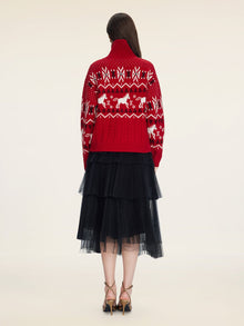A person faces away, wearing the Social Queen Playful Motif 100% Wool Cardigan in red and white, paired with a black layered tulle skirt and beige high-heeled sandals against a plain background.