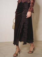 A person wears Social Queen’s Pleated Lace-Panel Velvet Skirt in brown with metallic heeled sandals and a small gold handbag, standing against a neutral background.