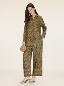 A woman wearing the Social Queen Printed Linen Blouse, paired with gold sandals and a woven handbag, accessorized with jewelry, stands against a plain background.