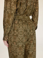 A person is shown from the back wearing Social Queen’s Printed Linen Straight-Leg Pants in olive green and brown with an intricate floral pattern, paired with a coordinating long-sleeve top.