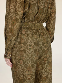 A person is shown from the back wearing Social Queen’s Printed Linen Straight-Leg Pants in olive green and brown with an intricate floral pattern, paired with a coordinating long-sleeve top.