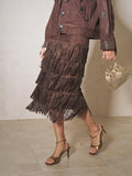 A person wearing the Social Queen Rhinestone Fringe Suede Midi Skirt, paired with a matching studded jacket, gold heeled sandals, and a small gold handbag.