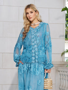A woman in the Social Queen Rose Appliqué 100% Mulberry Silk Blouse with romantic puff sleeves and a matching skirt stands against a white stone wall, holding a beige beaded handbag and wearing a choker necklace.