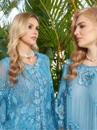 Two women, both wearing pearl necklaces, stand in front of lush green tropical plants; one wears the Social Queen Rose Appliqué 100% Mulberry Silk Blouse and the other dons an embroidered gown.