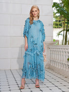 A woman stands on a tiled patio wearing the Social Queen Rose Appliqué 100% Mulberry Silk Dress, holding a small handbag and wearing heeled sandals.