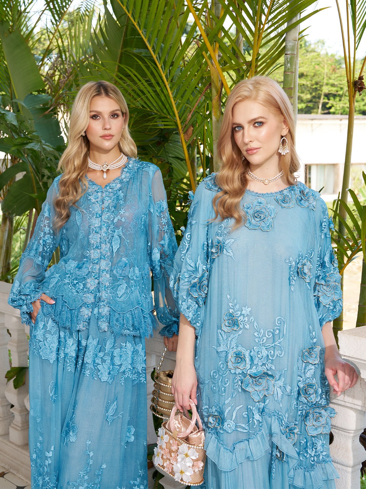 Two women stand outdoors by green plants, wearing Social Queen Rose Appliqué 100% Mulberry Silk Dresses with jewelry. One holds a decorative handbag.