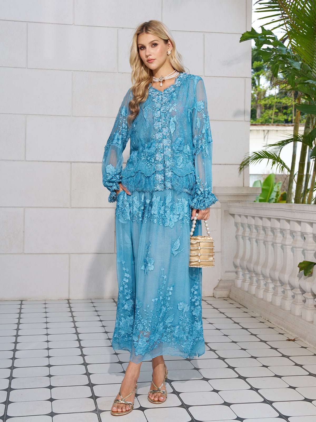 A woman on a tiled patio wears the Social Queen Rose Appliqué 100% Mulberry Silk Skirt, styled with sandals, layered jewelry, and a gold purse.