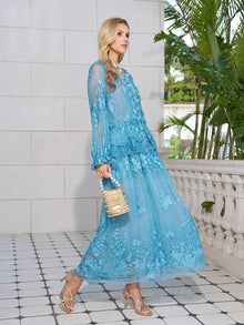 A woman in the Social Queen Rose Appliqué 100% Mulberry Silk Skirt and strappy heels holds a small woven handbag, standing on a tiled patio surrounded by plants.