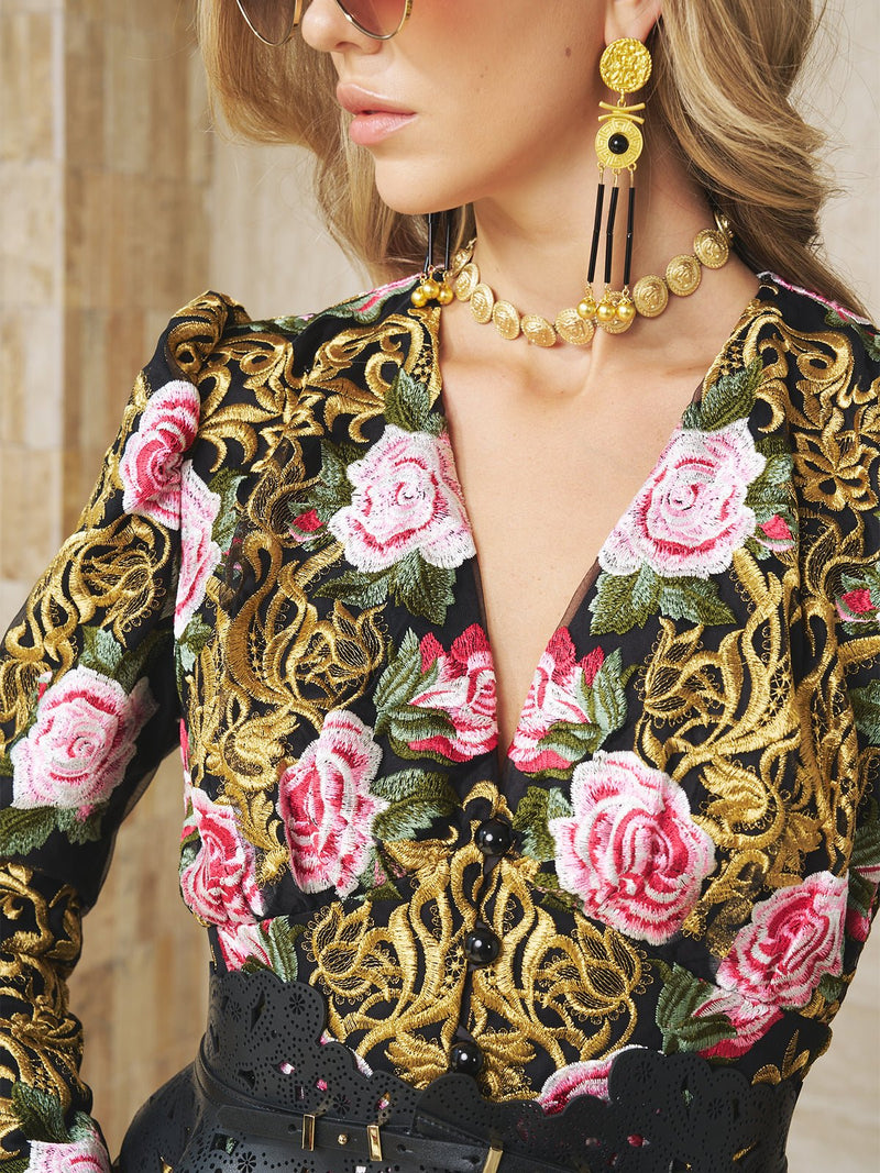 A woman in sunglasses and gold jewelry wears the Social Queen Rose Embroidered Lace Gown, featuring a black upper bodice with pink 3D roses and gold Baroque motifs. Only her upper body is shown.