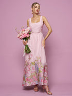 A woman in the Social Queen Rose Jacquard Sleeveless Gown with crystal trim holds a pink bouquet against a pink background.