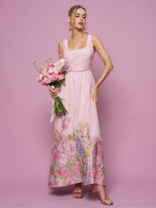 A woman in the Social Queen Rose Jacquard Sleeveless Gown with crystal trim holds a pink bouquet against a pink background.