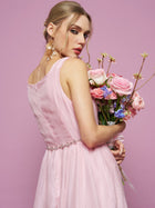 A woman in the Social Queen Rose Jacquard Sleeveless Gown, featuring crystal-embellished trim, holds a bouquet while standing gracefully against a solid pink background.