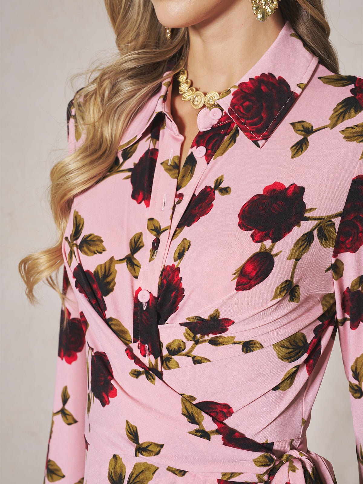 A woman models the Social Queen Rose Print Knit Dress in pink, paired with gold earrings and a gold necklace; her head is partially out of frame.