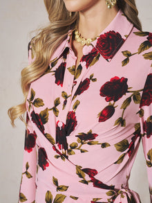 A woman models the Social Queen Rose Print Knit Dress in pink, paired with gold earrings and a gold necklace; her head is partially out of frame.