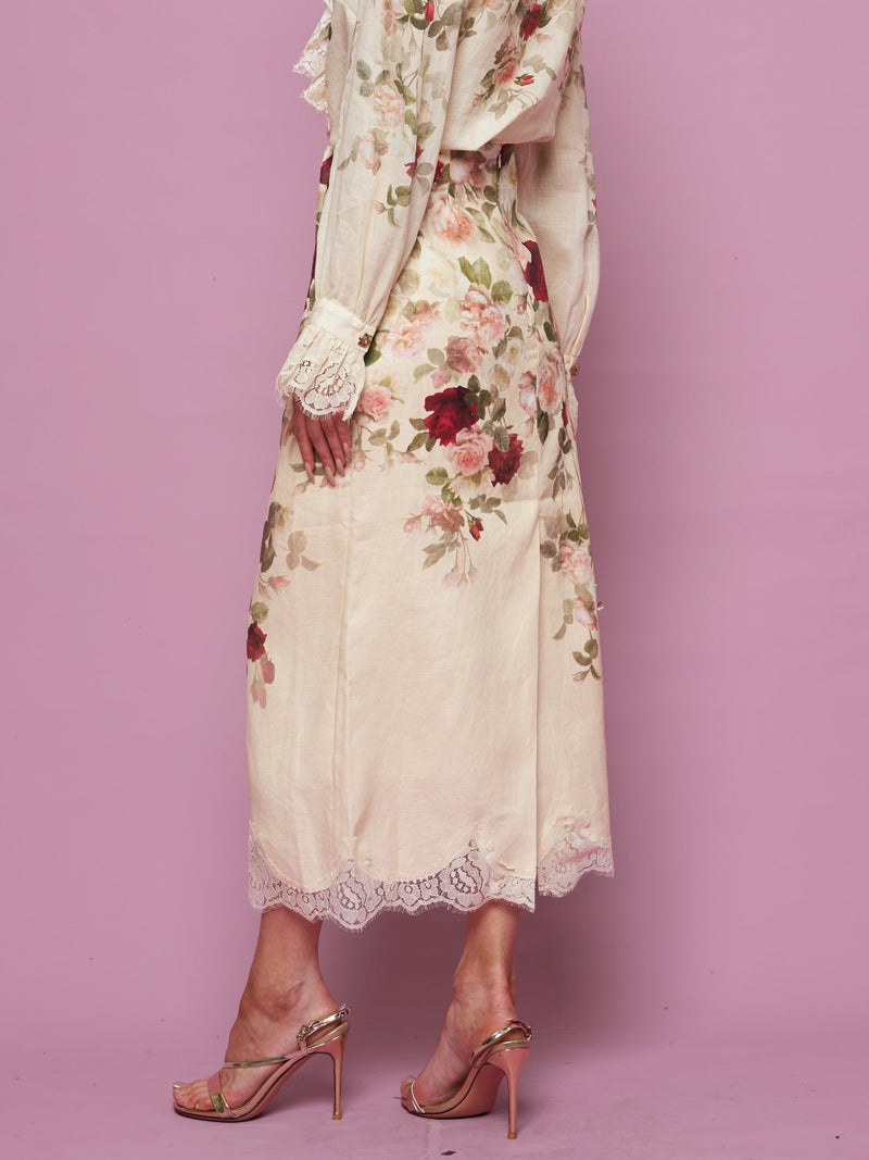 A person wearing the Social Queen Rose Print Lace Hem Linen Skirt and metallic high-heeled sandals stands against a pink background.