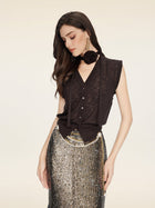 A woman in the Social Queen Rose-Tie Neck Knit Cardigan and a sequined silver skirt with chain belt, large earrings, and a floral neck accessory looks downward against a plain background.