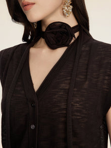 A woman wears the Social Queen Rose-Tie Neck Knit Cardigan, styled with a black fabric flower choker and gold dangling earrings.