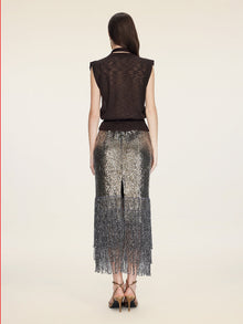 A woman stands with her back to the camera in a Social Queen Rose-Tie Neck Knit Cardigan and a silver sequin skirt with fringe, set against a plain beige background.