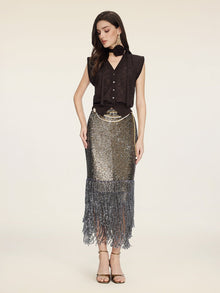 A woman wears the Social Queen Rose-Tie Neck Knit Cardigan, paired with a metallic sequined fringe skirt, gold heels, and a black scarf against a plain light background.