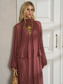A woman wears the Social Queen Ruched High-Neck Ruffled Midi Dress with a gold statement necklace and holds a beige handbag indoors.
