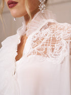 Close-up of a woman wearing the Social Queen Ruffled Lace Blouse with Asymmetric Hem, featuring organza ruffles at the collar and pearl earrings; only part of her face and upper body are visible.