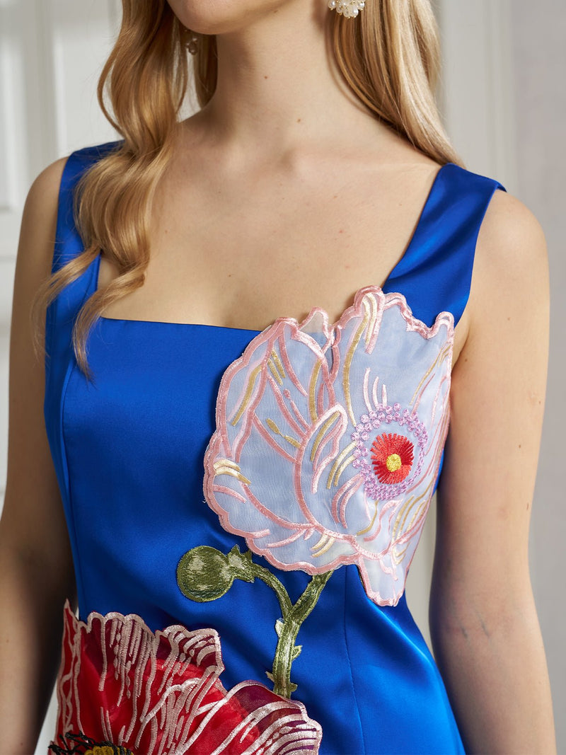 A woman wears Social Queen's Sculptural Floral Appliqué Satin Dress, a striking blue piece with bold 3D floral appliqué in pink, white, and red on the front.
