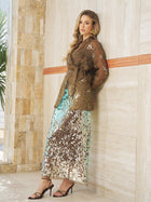 A woman wears Social Queen's Sequin Back-Slit Midi Skirt with a sheer brown belted top, strappy heels, and gold earrings, standing against a tiled wall.