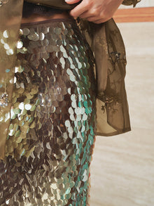 A close-up of a person wearing the Social Queen Sequin Back-Slit Midi Skirt with sheer, embroidered fabric, one hand resting on their waist.
