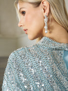 A woman with blonde hair is seen in profile wearing the Social Queen Sequin Cape Gown with Radiant Beaded Fringe, styled with dangling pearl earrings.