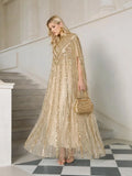 At a formal event, a woman stands on stairs in Social Queen's Sequin Cape Gown with Radiant Beaded Fringe, paired with a matching embellished handbag and gold strappy heels.