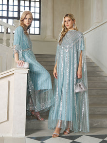 Two women wear Social Queen's Sequin Cape Gown with Radiant Beaded Fringe, posing on a staircase in an elegant, well-lit interior.