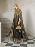 A woman stands on a staircase wearing Social Queen’s Sequin Cape Gown with Radiant Beaded Fringe, paired with a gold handbag, gold heels, and gold earrings.