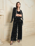 A woman poses indoors wearing the Sequin & Crystal Fringe Cardigan by Social Queen, styled as eveningwear with matching wide-leg pants, a black top, heeled sandals, and a small shoulder bag.