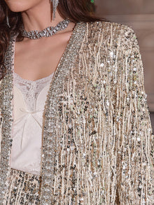 A woman wears Social Queen's Sequin & Crystal Fringe Cardigan over a cream lace top; diamond-trimmed edges, a beaded choker, and dangling earrings complete her versatile look.