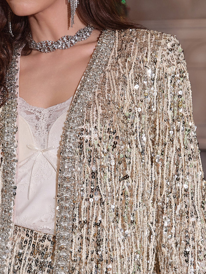 A woman wears Social Queen's Sequin & Crystal Fringe Cardigan over a cream lace top; diamond-trimmed edges, a beaded choker, and dangling earrings complete her versatile look.