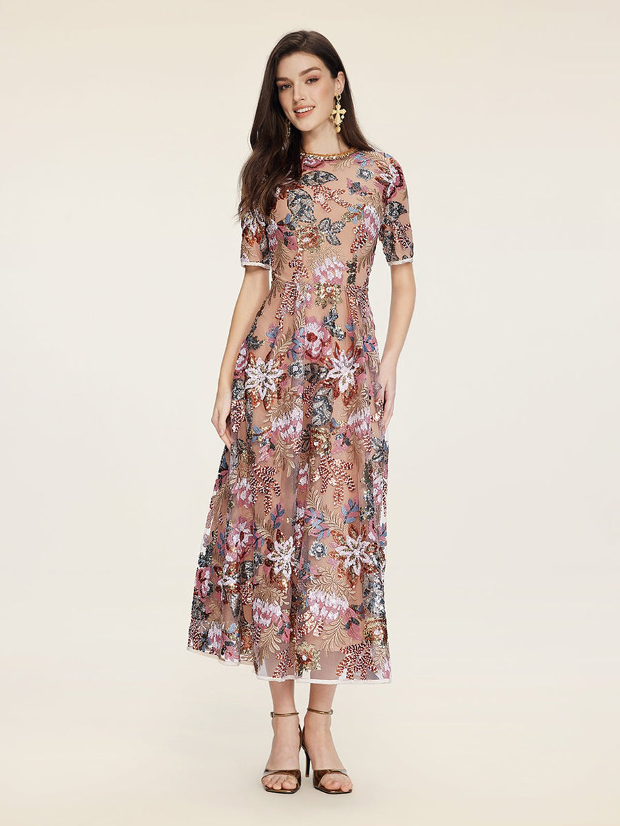 A woman wears the Social Queen Sequin Embellished Floral Dress, featuring short sleeves and floral details, styled with sandals against a plain light background.