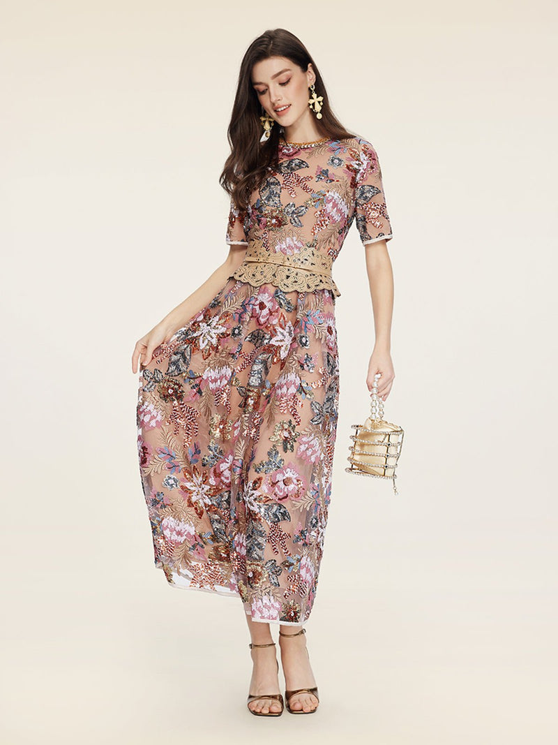 A woman models the Social Queen Sequin Embellished Floral Dress, featuring short sleeves and floral details. She accessorizes with a metallic handbag, strappy heels, and statement earrings—an elegant option for wedding guests.