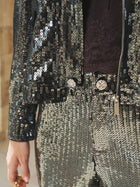 Close-up of a person wearing the Sequin-Embellished Metallic Crop Jacket by Social Queen, partially unzipped, paired with matching pants; hand resting at their side.