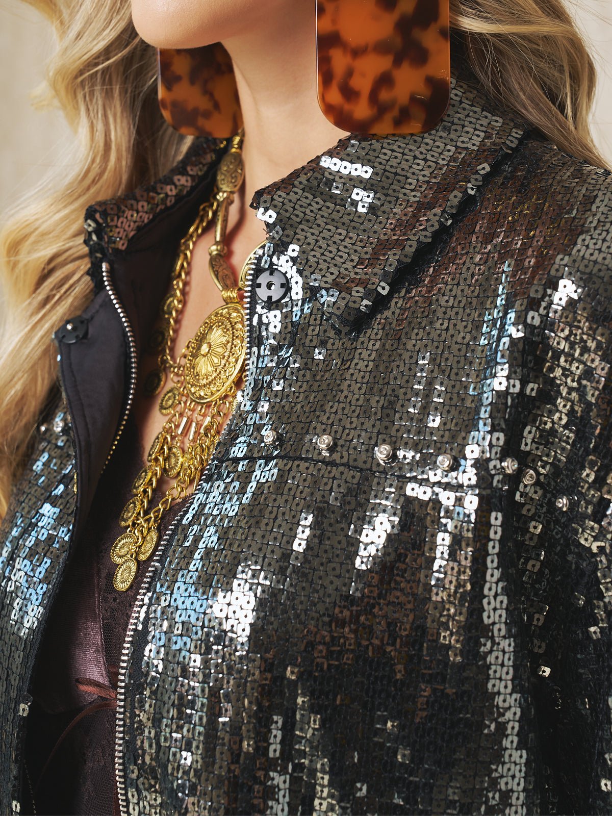 Close-up of a person wearing the Social Queen Sequin-Embellished Metallic Crop Jacket, paired with large tortoiseshell earrings and layered gold necklaces.