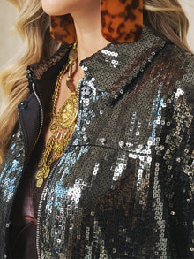 Close-up of a person wearing the Social Queen Sequin-Embellished Metallic Crop Jacket, paired with large tortoiseshell earrings and layered gold necklaces.