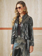 A woman in the Social Queen Sequin-Embellished Metallic Crop Jacket, gold earrings, sunglasses, and wavy hair poses against a beige tiled wall.