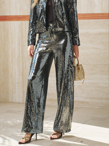 A person in Social Queen Sequin-Embellished Wide-Leg Pants pairs them with black high-heeled sandals and a small gold handbag, standing indoors against a light-colored wall.