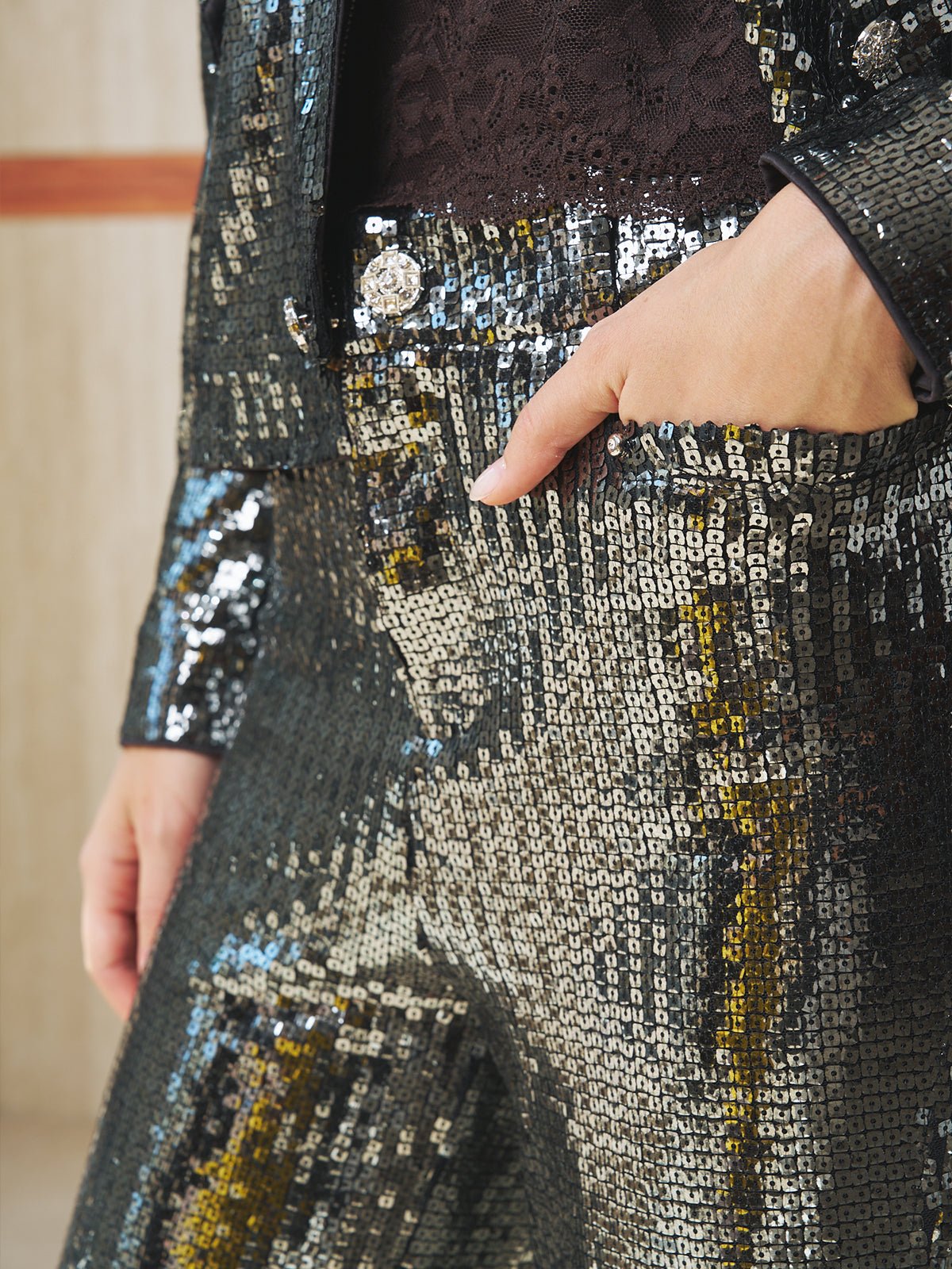 A person models Social Queen’s Sequin-Embellished Wide-Leg Pants—a shiny black and silver pair—paired with a matching suit, one hand casually placed in their pants pocket.