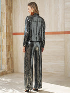 A woman stands indoors with her back to the camera, wearing Social Queen's Sequin-Embellished Wide-Leg Pants, paired with a shiny black sequin jacket, black heels, and large earrings.