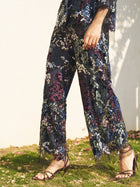 Standing outdoors in sunlight and shadows, the person wears Social Queen's Sequin Embroidered Mesh Wide-Leg Pants with a high waist and strappy sandals.